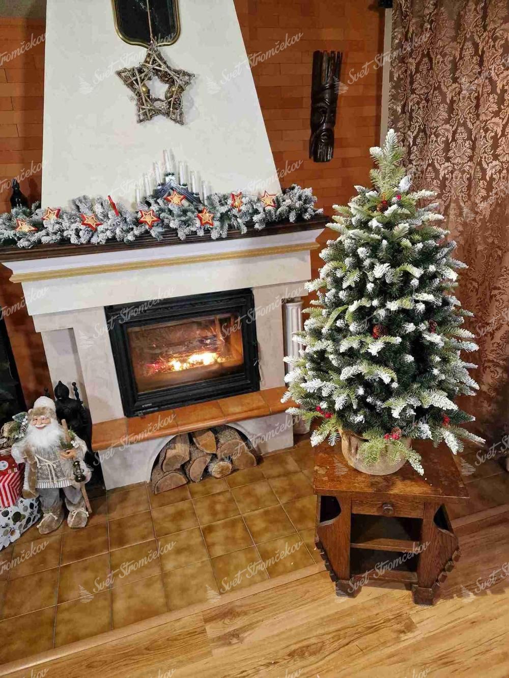 Vianočný stromček v kvetináči 3D Jedľa Zasnežená, stromček má zasnežené konce vetvičiek a je ozdobený šiškami ačervenými plodmi, je osadený v jutovom kvetináči