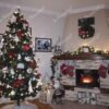 Ein hoher künstlicher Weihnachtsbaum mit schneebedeckten Enden der Zweige, geschmückt mit rot-weißen Weihnachtsdekorationen, im Wohnzimmer neben dem Kamin