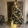 Ein hoher künstlicher Weihnachtsbaum mit schneebedeckten Enden der Zweige, geschmückt mit weißem und silbernem Weihnachtsschmuck, im Wohnzimmer