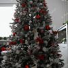 Ein schneebedeckter künstlicher Weihnachtsbaum, dicht mit rot-weißem Weihnachtsschmuck geschmückt, im Wohnzimmer,