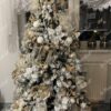 Ein künstlicher Weihnachtsbaum mit schneebedeckten Ästen, stark geschmückt mit weißem und goldenem Weihnachtsschmuck, im Wohnzimmer,