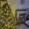 Grüner künstlicher Weihnachtsbaum mit versilberten Zweigenden und Eiskristallen, geschmückt mit weißem und goldenem Weihnachtsschmuck, im Wohnzimmer, am Kamin
