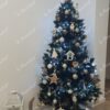 Ein grüner künstlicher Weihnachtsbaum mit versilberten Zweigenden und Eiskristallen, geschmückt mit weißem und goldenem Weihnachtsschmuck, im Wohnzimmer,