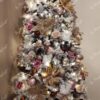 Ein verschneiter künstlicher Weihnachtsbaum, geschmückt mit rosa-weiß-goldenem Weihnachtsschmuck, im Wohnzimmer
