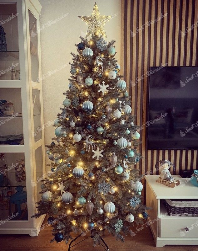 Umelý vianočný stromček s ľadovo-zelenými vetvičkami, ozdobený bielo-zlatými ozdobami.