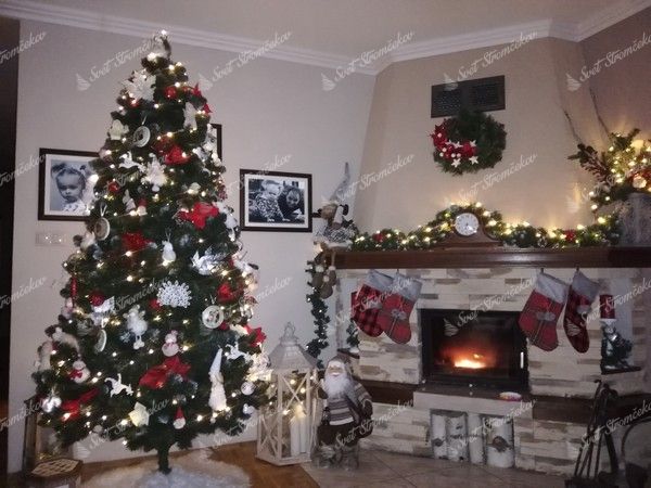 Umelý vianočný stromček so zasneženými koncami vetvičiek s bielo-červenými vianočnými ozdobami, pri krbe v obývačke